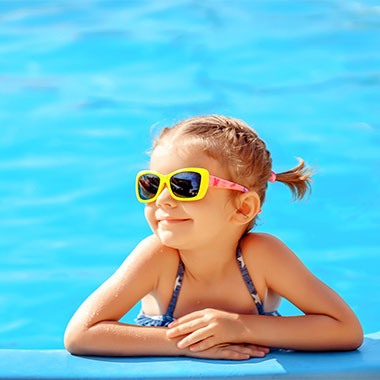 Uma criança sorri à beira de uma piscina. A dureza da água nas piscinas pode danificar as superfícies da piscina e corroer os tubos.
